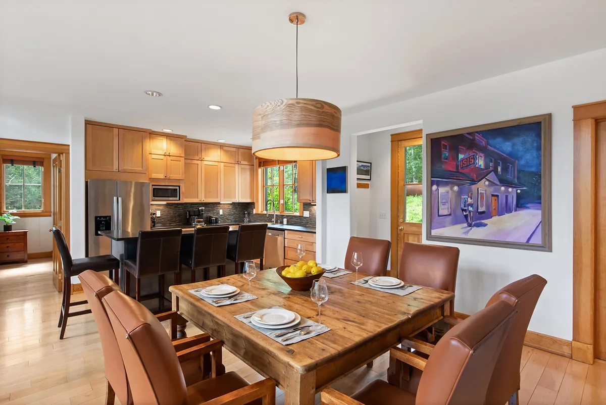 A cozy wooden dining table sits adjacent to the kitchen, set for family gatherings and surrounded by stylish cabinetry and artwork. The scene evokes togetherness, celebration, and the making of culinary memories—core elements of the gathering hub experience.