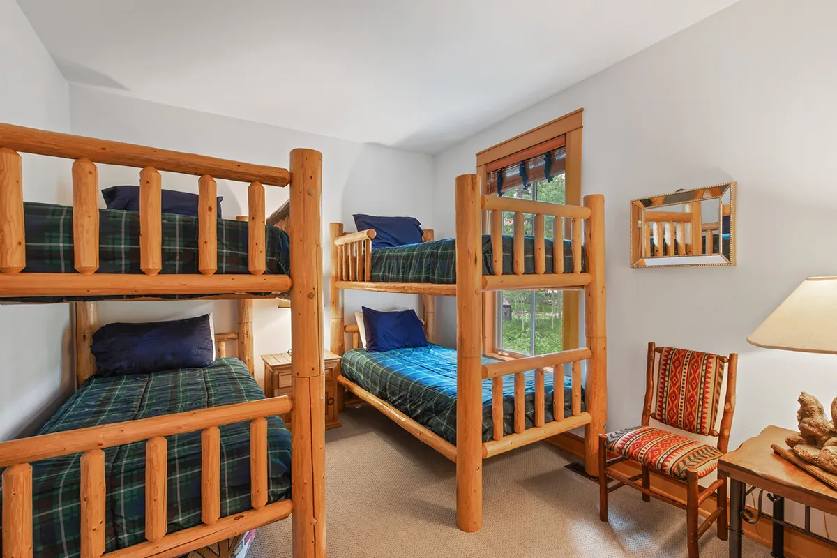A playful bunk room with sturdy wooden bunk beds, a colorful chair, and a window offering pleasant views. The space is lively yet relaxed, ideal for children to enjoy sleepovers, games, or bedtime stories.