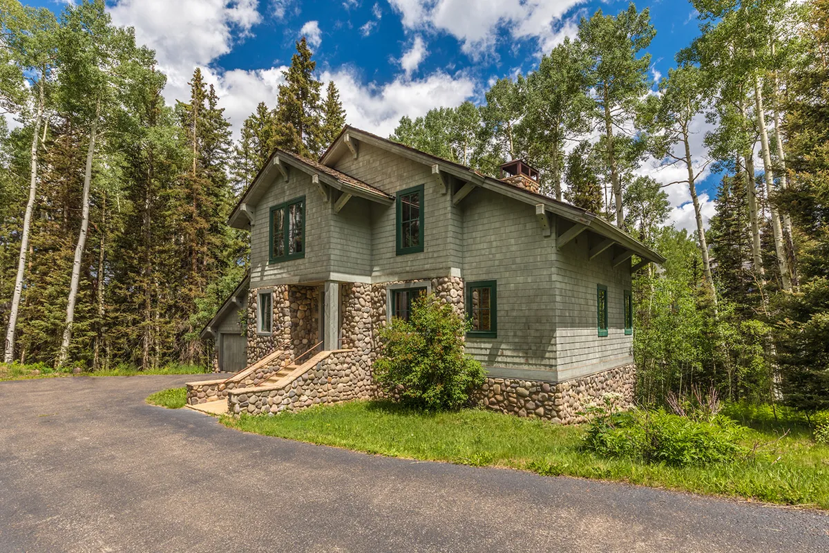 This exterior image showcases the chalet’s stone foundation, expansive windows, and the privacy offered by surrounding mature trees. The peaceful setting is accentuated by a tranquil porch, ideal for enjoying morning coffee or evening sunsets, reflecting the serene atmosphere and private setting described in the section.