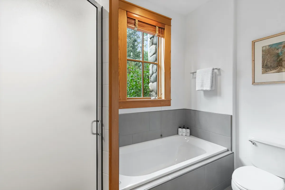 A serene bathroom with a bathtub next to a window, framed artwork, and a towel rack. The tranquil scene is perfect for enjoying a warm bath with views of nature.